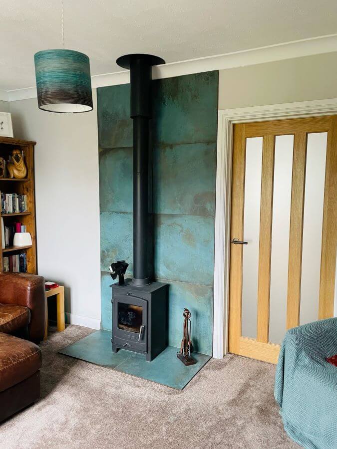 FORGE-MINT-STOVE. Image shows green metallic tiles at back of a wood burning stove
