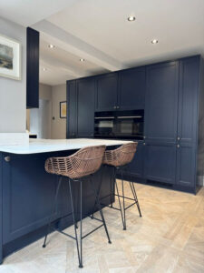 Louis porcelain floor tile that looks like wood, image shows a dark blue kitchen, white worktops and wood effect floor tiles.