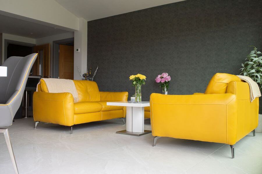 HAVEN-STONE-KITCHEN. Image shows mustard yellow sofas with dark grey wall in background on stone effect large tiles
