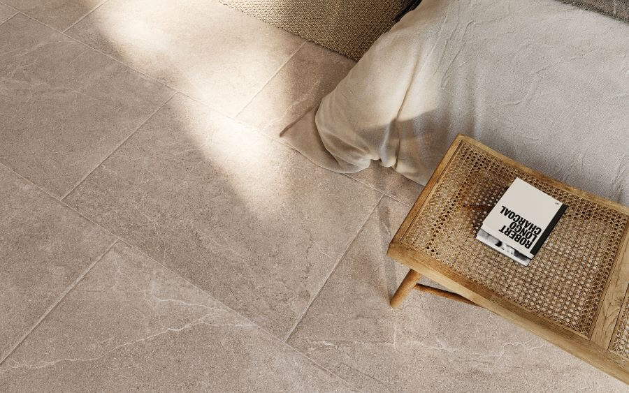 BLISS-FLAGSTONE-EFFECT-PORCELAIN-CARAMEL. Image shows caramel 900 x 600mm flagstone effect porcelain close up with table and edge of bed