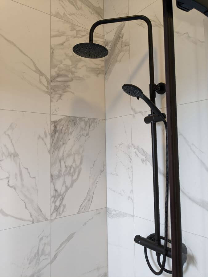 CARERRA-ARGENT-SHOWER. Image shows white marble tiles with light grey veining in shower with matt black shower head