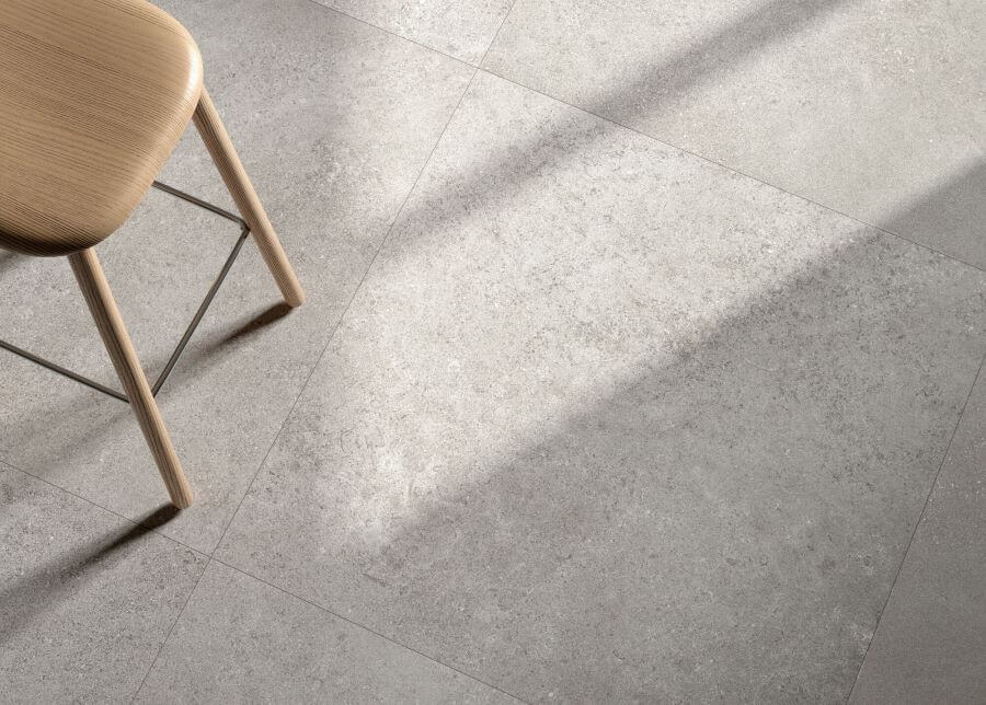 CHIC-SILVER-LIMESTONE-LOOK-PORCELAIN-TILE-1. Image shows close up of silver limestone look porcelain tile in a kitchen with a wooden stool