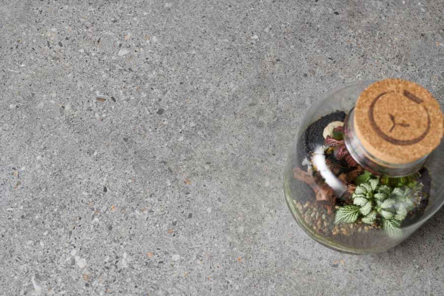 DEFINE-GREY-TERRAZZO-EFFECT-PORCELAIN-TILE-CLOSEUP. Image shows grey terrazzo effect porcelain tile with plant
