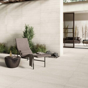 ETHOS-SHORE-STONE-LOOK-PORCELAIN-TILE-OUTSIDE-RECLINER. Image shows stone look porcelain tile outside. Image shows cream stone look porcelain tile outside with brown lounger and table