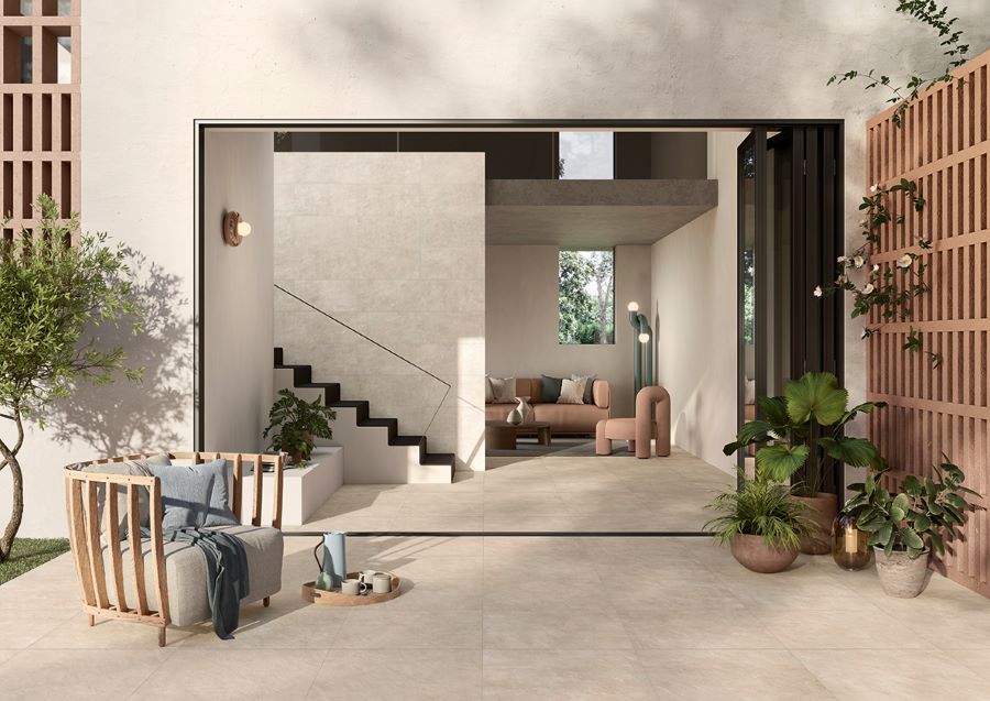 Image shows Minima concrete effect porcelain outdoor tiles in sand on patio with plants and chair looking into lounge