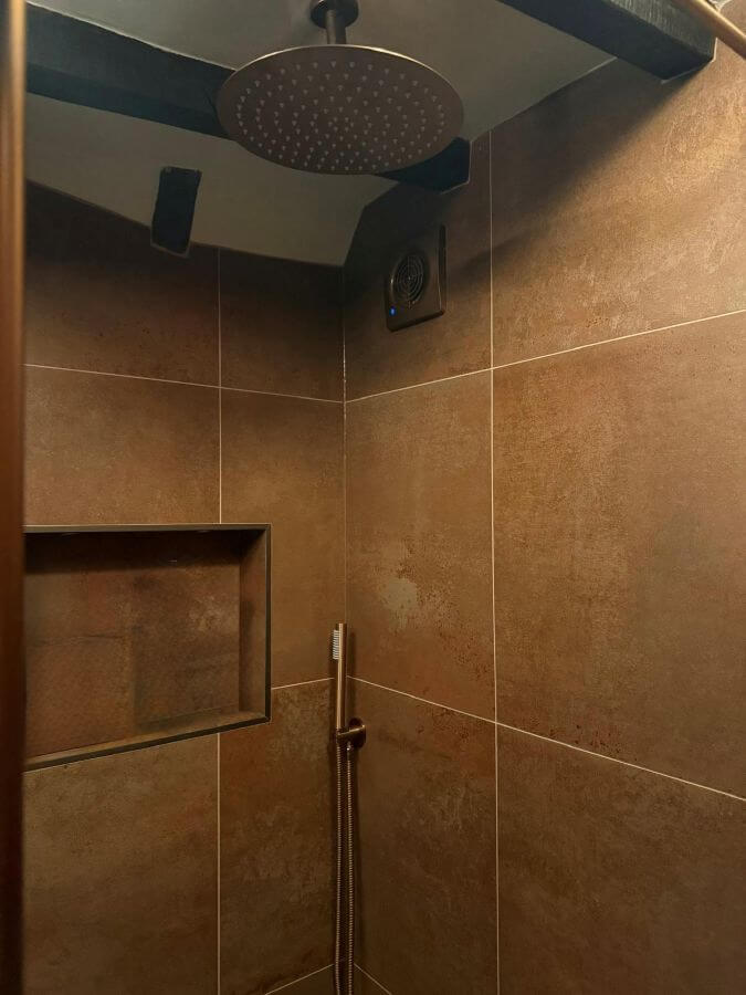 Stunning bathroom feature wall using 600x600 Etch Metal Bronze tiles, showcasing the light-reflecting metallic surface and deep bronze hues.